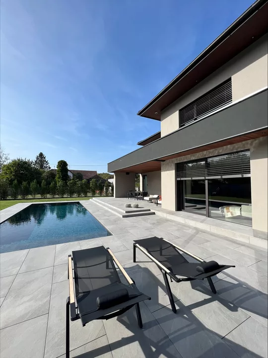 Baies vitrées équipées de brise-soleil orientables sur une maison contemporaine avec terrasse et piscine.