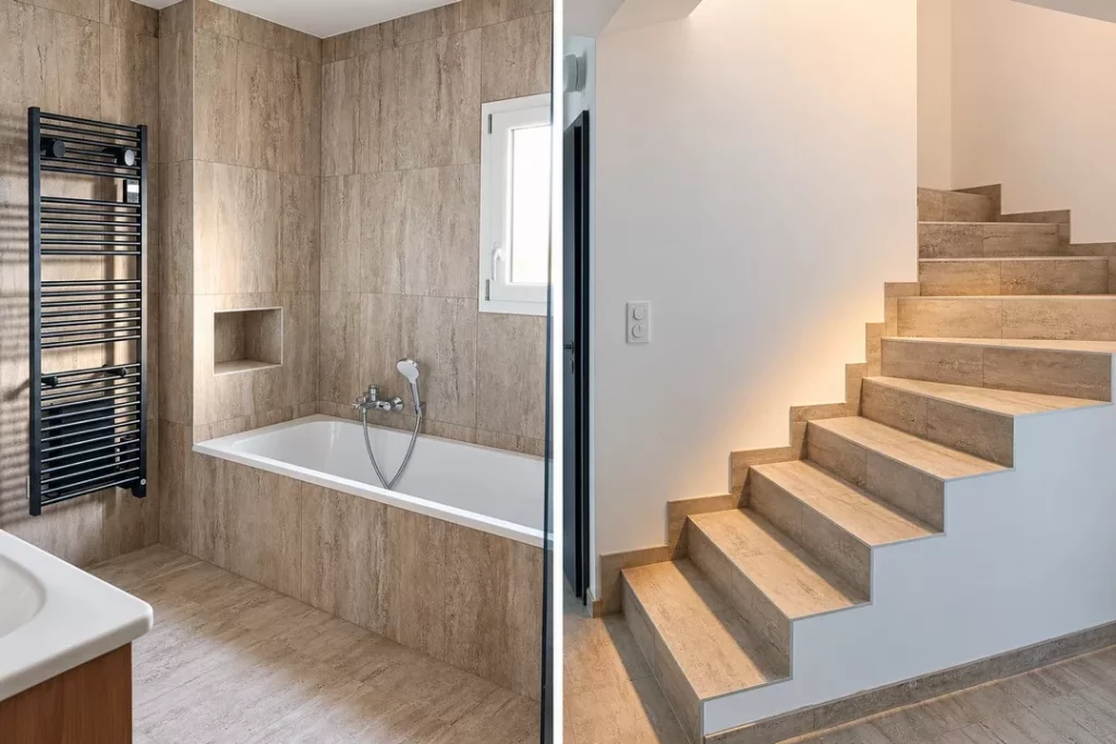 Salle de bains avec baignoire et sèche-serviettes noir, à côté d’un escalier carrelé aux murs