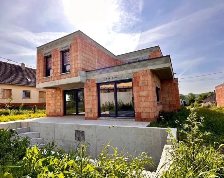 Maison contemporaine à toit plat en briques apparentes, avec grandes baies vitrées anthracite et terrasse en béton brut.