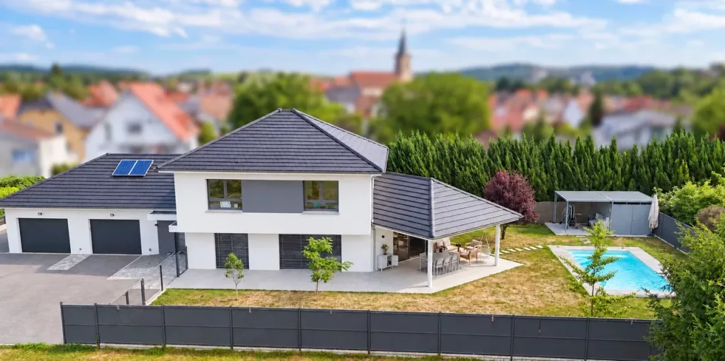Vue aérienne d’une maison à quatre pans avec double garage, terrasse couverte, jardin et piscine.